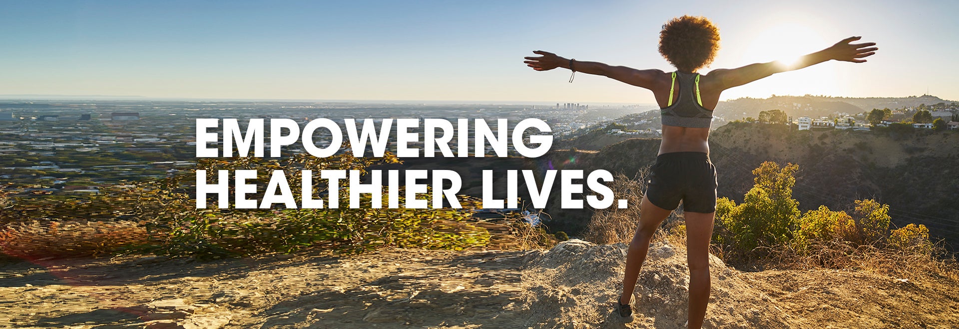 Empowering healthier lives with a women standing on top of a mountain lookout. 